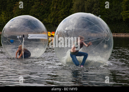 Zwei junge Mädchen spielen in einem Bubblerunner über den öffentlichen See bei Rouken Glen Park, Glasgow, UK, Schottland Stockfoto