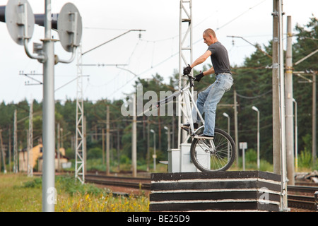 Junger Mann auf Betonsteinen ohne Vorderrad im Stadtgebiet mit der Eisenbahn im Hintergrund stehen. Niedrigen Winkel Ansicht. Stockfoto