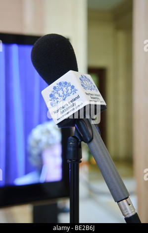 Mikrofon mit "Northern Ireland Assembly" vor einem TV-Bildschirm zeigt Berichterstattung aus der Exekutive Kammer Stockfoto