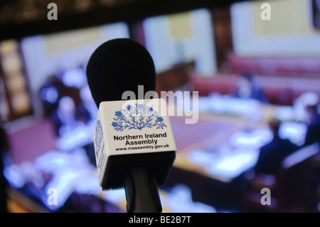 Mikrofon mit "Northern Ireland Assembly" vor einem TV-Bildschirm zeigt Berichterstattung aus der Exekutive Kammer Stockfoto