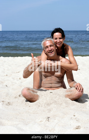 Attraktives Paar am Strand sitzen. Gut aussehender Mann Daumen aufgeben Stockfoto