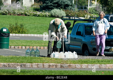 Mann und Frau Kunststoff Krüge mit Frischwasser aus einem outdoor Wasserhahn Zapfen zu füllen. Stockfoto