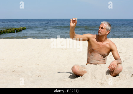 Gut aussehender Mann am Strand hält Stein sitzen Stockfoto