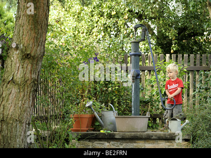 Ein drei Jahre alter Junge spielt mit einem Outdoor-Vintage Hand Wasser Pumpe Garten Stockfoto