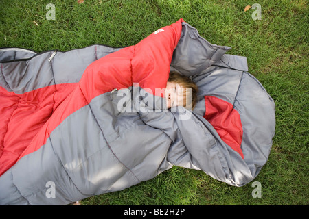 sieben Jahre alter Junge in einem Schlafsack im Freien in einer Wiese zur Festlegung Stockfoto