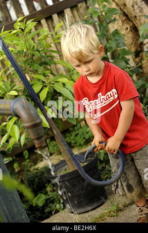 Ein drei Jahre alter Junge spielt mit einem Outdoor-Vintage Hand Wasser Pumpe Garten Stockfoto