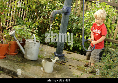 Ein drei Jahre alter Junge spielt mit einem Outdoor-Vintage Hand Wasser Pumpe Garten Stockfoto