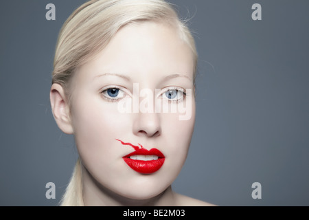 Porträt einer jungen blonden Frau mit Lippenstift Blutungen über ihre Lippen mit Blick auf den Betrachter, unvollkommen, Schönheit Stockfoto