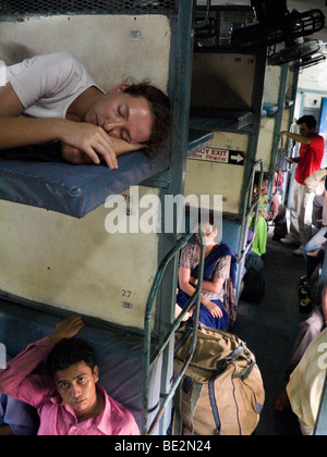 Westeuropäische Pkw ruht auf einem Sleeper Bett über indische Passagiere sitzen in einem Sleeper-Abteil. Indische Zug. Stockfoto