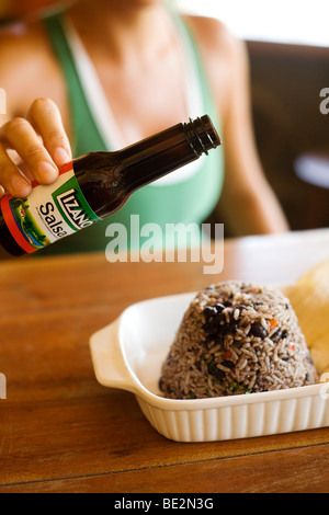 Lizano Sauce gegossen wird, auf einen Teller mit Gallo Pinto, eine typische und traditionelle Gericht in Costa Rica Stockfoto