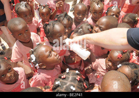 Schulkinder in Haiti warten auf einen Drink mit sauberem Wasser aus einer Entwicklungshelferin. Stockfoto