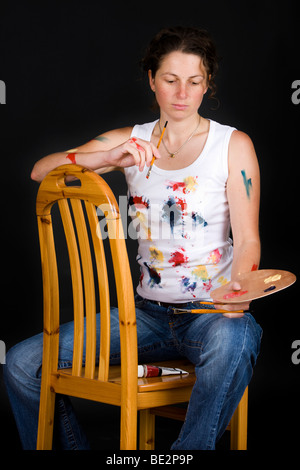 Künstler, die auf einem Stuhl sitzend hält eine Pinsel und Farbpalette, nachdenklich Stockfoto