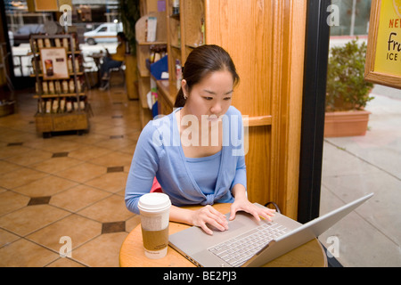 Koreanische Studentin sitzt am Tisch im Café Fenster auf Laptop-Computer mit Kaffeetasse am Tisch arbeiten Stockfoto