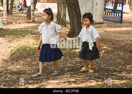 Eine junge weibliches Kind führt andere kleine Mädchen mit der hand über Hof von der Schule in Kambodscha Stockfoto