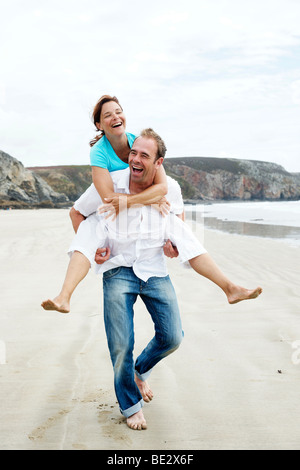 Ein Mann mit einer Frau Piggy back am Strand Stockfoto