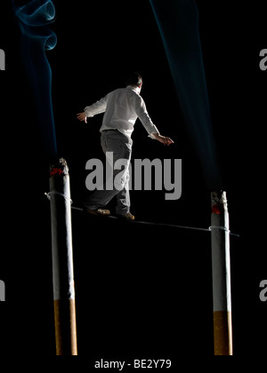 Ein Mann, eine Gratwanderung zwischen zwei großen Zigaretten ausgesetzt. Ein Konzeptbild über die gesundheitlichen Risiken des Rauchens. Stockfoto