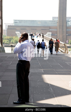 der Mensch steht während des Gesprächs auf dem Handy mit der Millennium Bridge und der Tate modern im Hintergrund Stockfoto