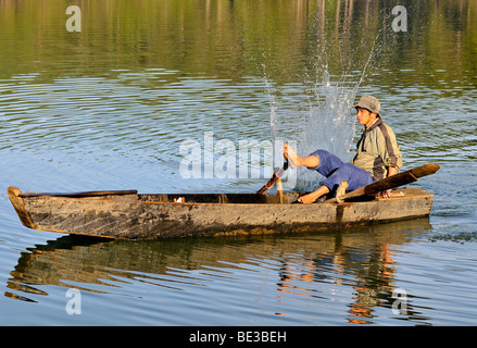 Fischer in einem hölzernen Angeln Boot mit der traditionellen Stick-Schlag-Methode, Tuyen Lam See, Dalat, Hue, Vietnam, Stockfoto