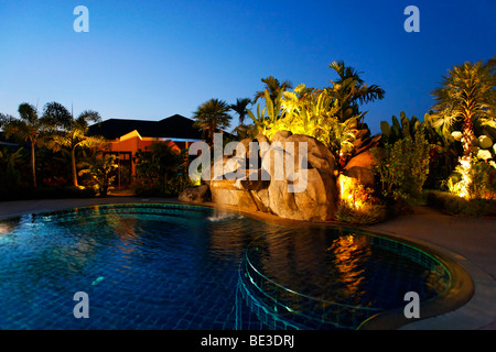 Beleuchtete Bungalow mit grünen, künstlichen Wasserfall und Pool in der Dämmerung, Palm Garden Resort, Khao Lak, Phuket, Thail Stockfoto