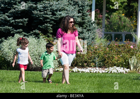 A Mutter ihren kleinen Sohn und ihrer kleinen Tochter auf dem Rasen im Garten der schönen Park spazieren. Stockfoto