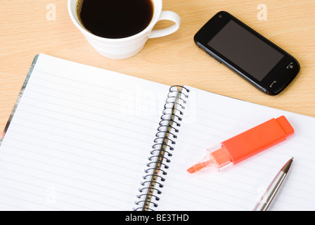 Handy mit Spiral-Notizbuch, Tasse Kaffee, Textmarker und Kugelschreiber auf Bürotisch angeordnet Stockfoto