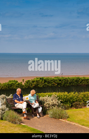 Zwei Rentner sitzen auf einer Strandpromenade Bank lesen Sie ihre Zeitung am Hunstanton, North Norfolk, Großbritannien Stockfoto