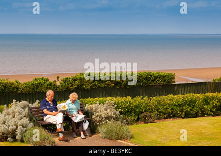 Zwei Rentner sitzen auf einer Strandpromenade Bank lesen Sie ihre Zeitung am Hunstanton, North Norfolk, Großbritannien Stockfoto