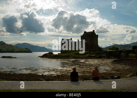 Eilean Donan Castle Hintergrundbeleuchtung mit Loch Duich und zwei Menschen sitzen vor Anzeige der Burg eine Birdis nach links fliegen Stockfoto