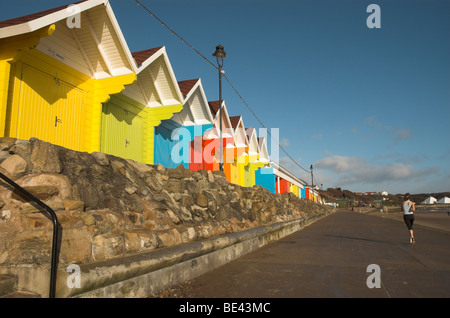 Bunte Strandhäuschen auf North Bay Scarborough mit Jogger Stockfoto