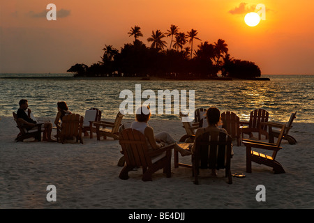 Menschen sitzen auf Stühlen am Strand mit Longdrinks vor einen goldenen Sonnenuntergang Malediven Insel, Rihiveli, Insel, Mald Stockfoto