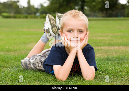 Porträt eines jungen Mannes, Lächeln, liegen mit gesenktem Kopf in seinen Händen auf dem Rasen in einem Park nahe Horizontal. Stockfoto