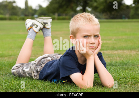 Porträt eines jungen Mannes ein böses Gesicht, liegen mit gesenktem Kopf in seinen Händen auf dem Rasen in einem Park nahe Horizontal. Stockfoto