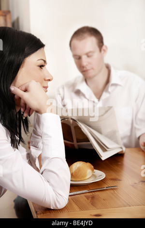 Junge Frau sitzt gelangweilt am Frühstückstisch, während er die Zeitung liest Stockfoto