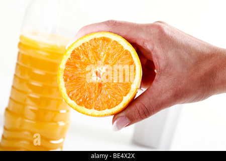 Hand mit halben Orange vor eine Flasche Orangensaft Stockfoto