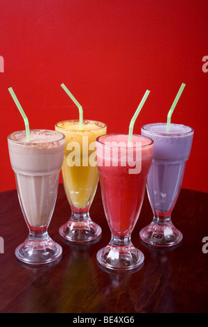 Vier coole Milchshakes gegen eine bunte Wand. Aromen sind Schokolade, Mango, Himbeeren und Heidelbeeren. Stockfoto