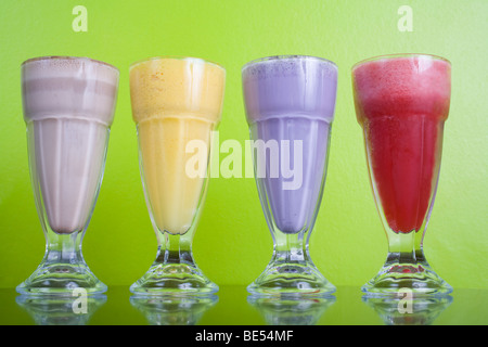 Vier coole Milchshakes gegen eine bunte Wand. Aromen sind Schokolade, Mango, Himbeeren und Heidelbeeren. Stockfoto