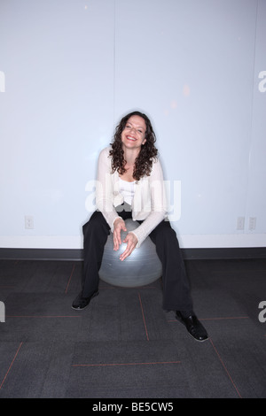 Frau sitzt auf Ball lächelt in die Kamera Stockfoto