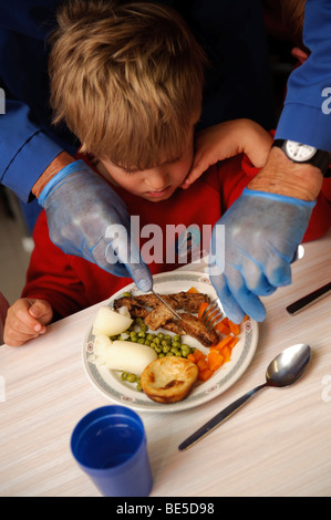 Erwachsenen mit blauen Latex Handschuhen schneiden das Essen für ein junges Kind Schule Abendessen in einer Grundschule, Wales UK Stockfoto
