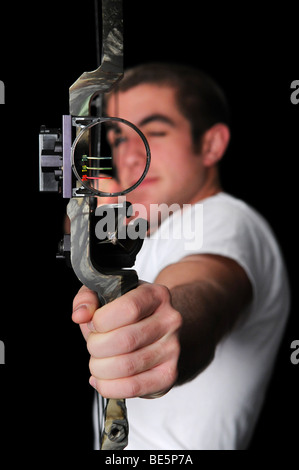 Junger Mann mit Bogen und Pfeil mit dem Ziel direkt über einen schwarzen Hintergrund isoliert. Stockfoto