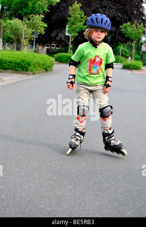 Mädchen mit Inline-Skates, ist 5 Jahre, auf der Straße durch einen Helm und Arm und Knie-Protektoren geschützt. Stockfoto