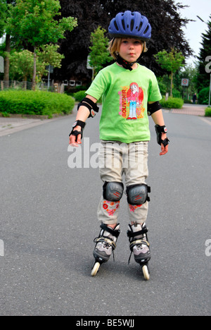 Mädchen mit Inline-Skates, ist 5 Jahre, auf der Straße durch einen Helm und Arm und Knie-Protektoren geschützt. Stockfoto