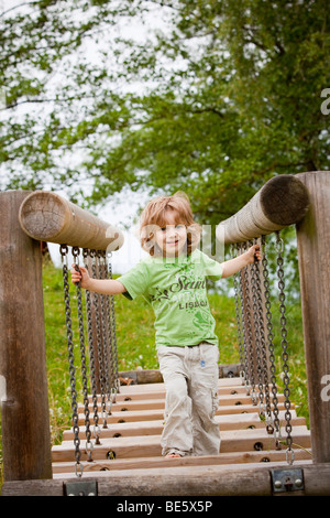 Junge, 3 Jahre alt, läuft über eine Kettenbrücke auf einem Spielplatz Stockfoto