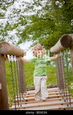 Junge, 3 Jahre alt, läuft über eine Kettenbrücke auf einem Spielplatz Stockfoto