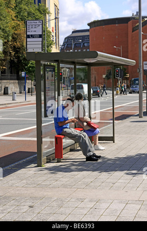 Mann mit seiner Freizeit auf SMS während der Wartezeit für einen Bus an einer Abholstelle in Bristol City England Stockfoto