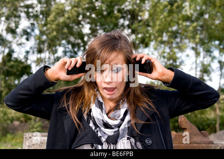 Eine verwirrt junge Dame, die darauf warten, auf ihr Handy und Multi-tasking mit zwei Handys zu vernetzen Stockfoto