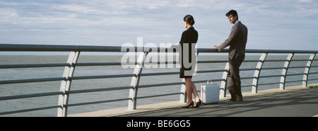 Berufskollegen an Uferpromenade Reling betrachten, Aktentasche auf Bürgersteig dazwischen Stockfoto