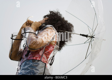 Junge Frau mit Regenmantel und Schirm im Regen stehen Stockfoto