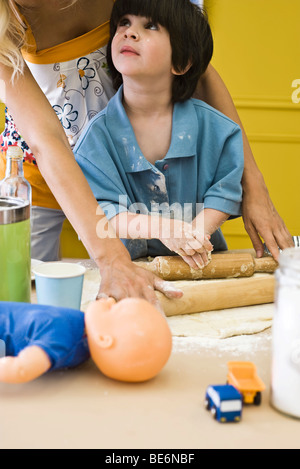 Junge ausrollen Teig mit Mutter, beschnitten Stockfoto