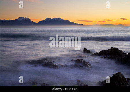 Wellen auf Felsen und Seaward Kaikoura Range an der Dämmerung, Kaikoura, Südinsel, Neuseeland Stockfoto