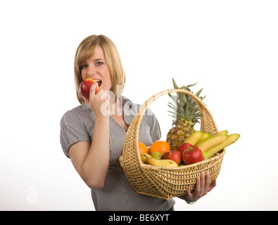 Junge Frau hält einen Korb mit Obst und in einen roten Apfel beißen Stockfoto